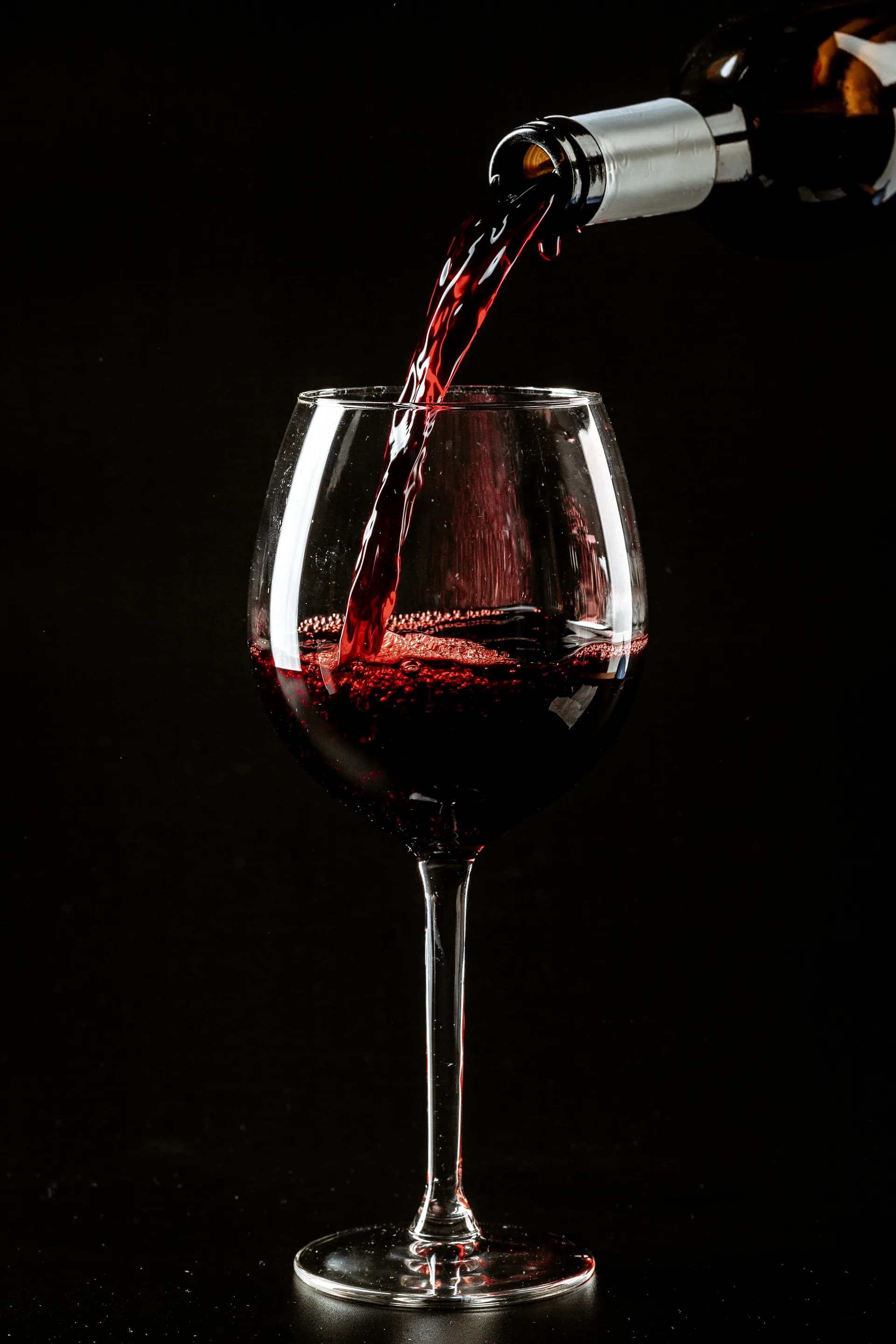 Red wine being poured into a wine glass against a dark background